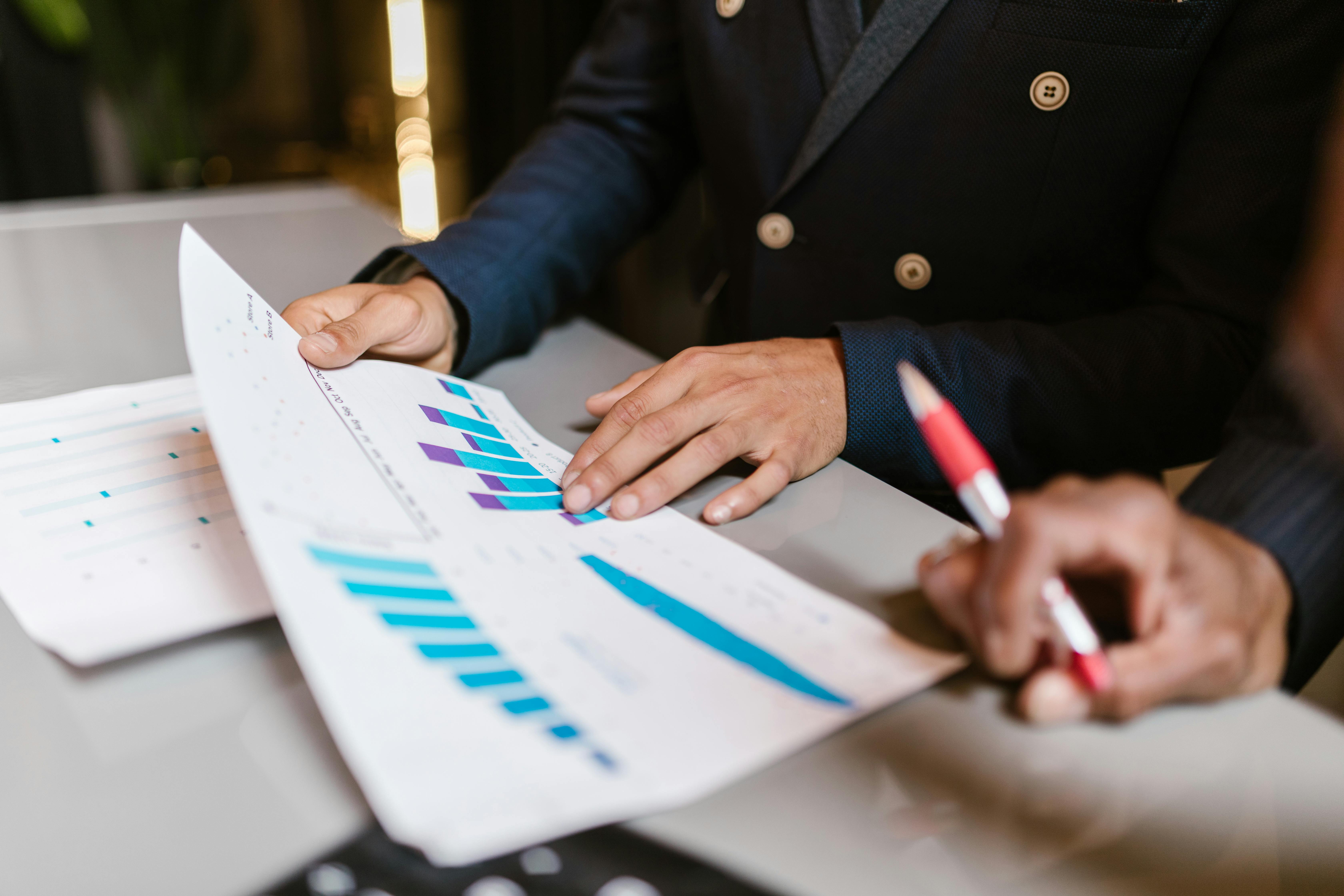Man in pak bekijkt financiële grafieken en rapporten met staafdiagrammen op papier.
