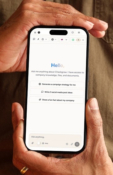 A man in a dark sweater and a woman in glasses wearing a navy blouse sit together at a desk, smiling at the camera with a laptop in front of them.
