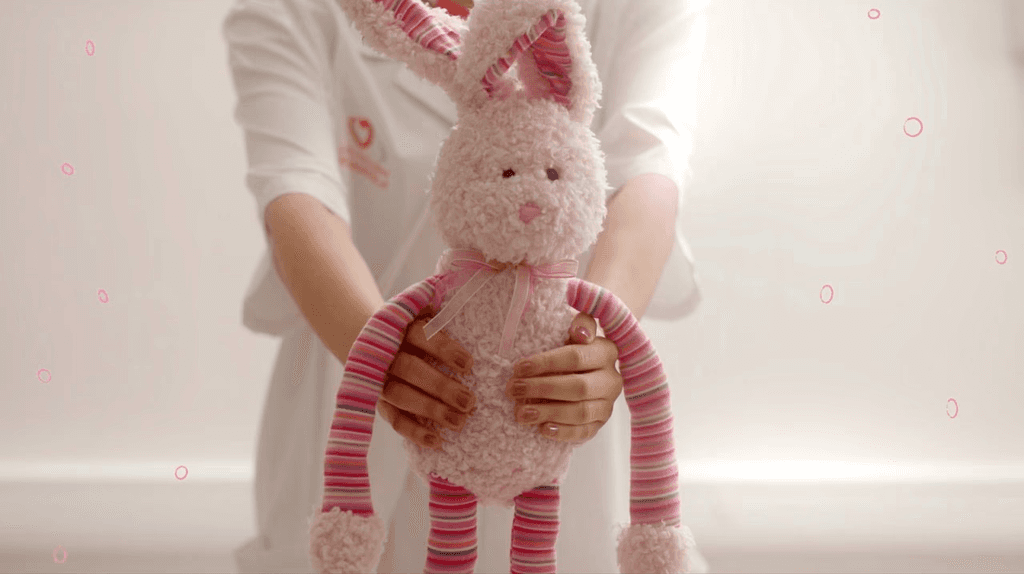 Screenshot from the ad, showing the doctor handing the stuffed bunny to the little girl. There are some floating hand-drawn bubbles around (my animations.)
