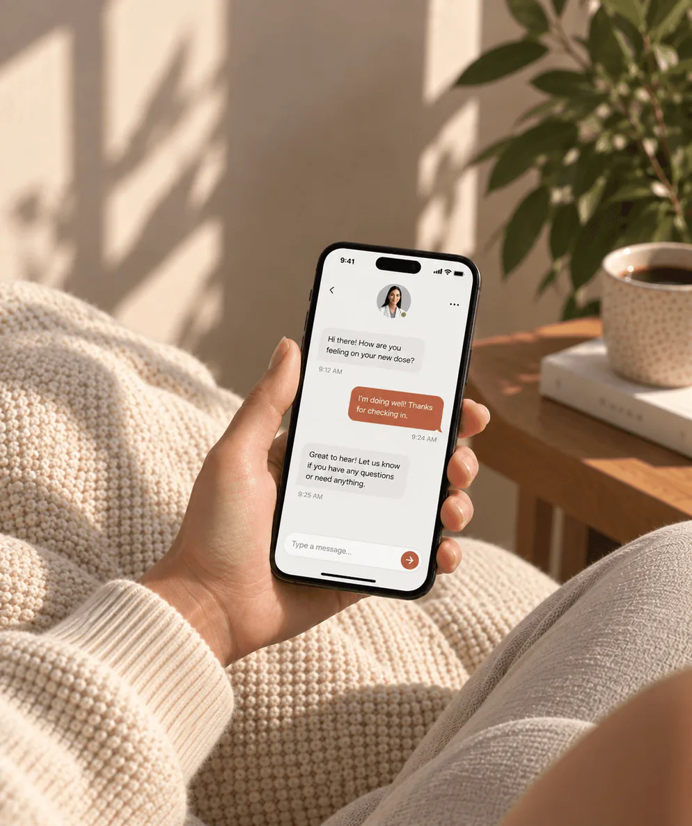 A hand holding a phone open on a message thread, a knit blanket and houseplant behind