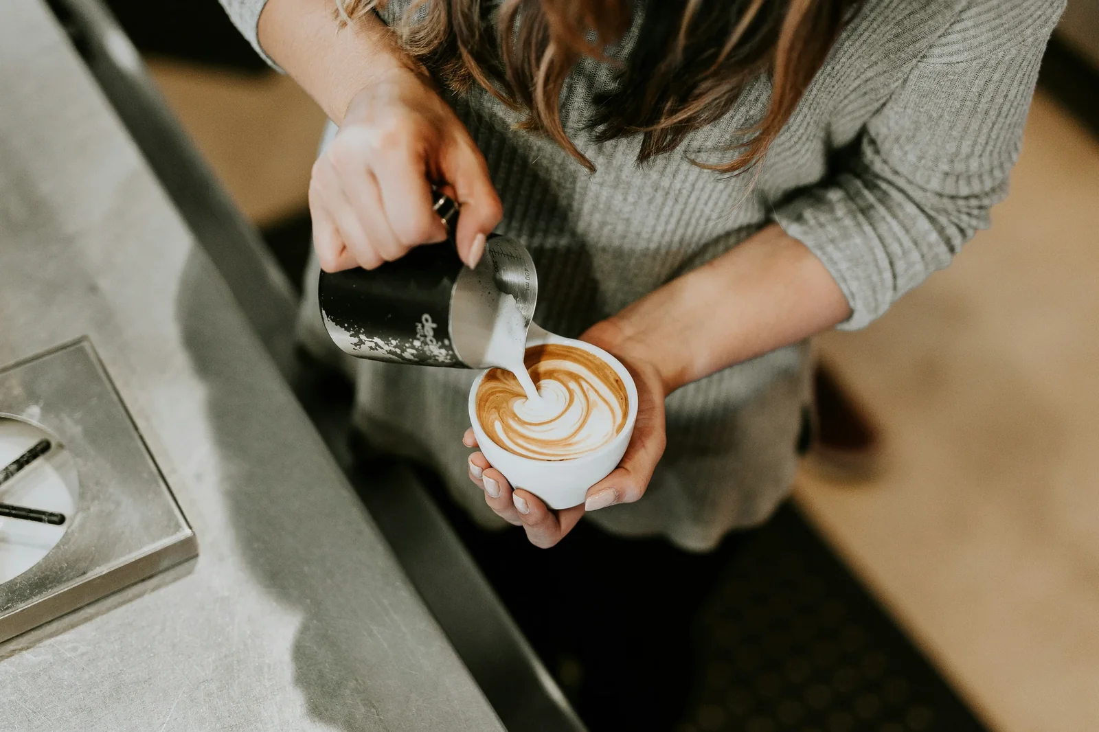 Barista pouring steamed milk into espresso cup to create latte art in café setting.