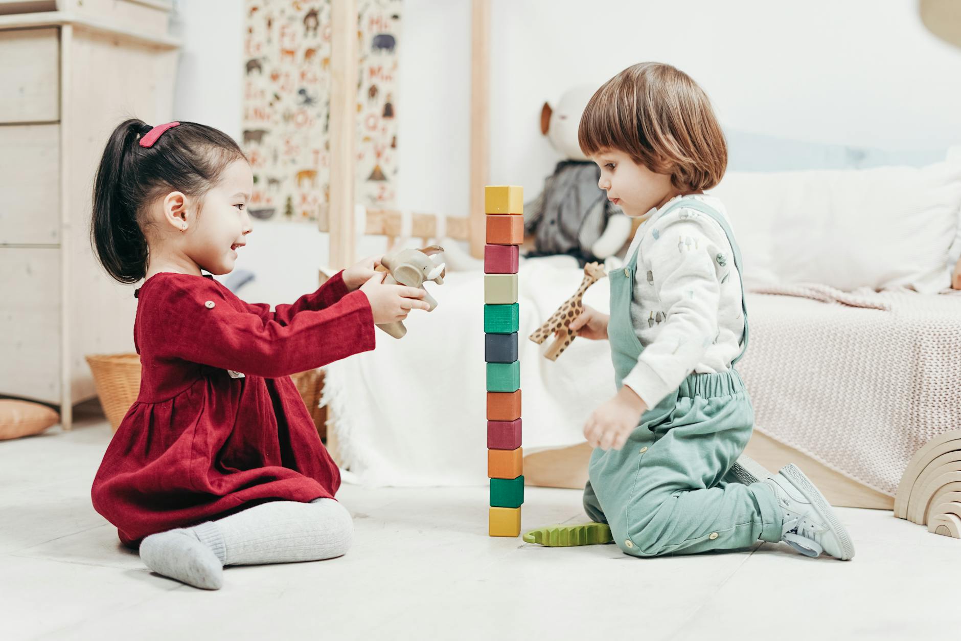 Two children sitting on the floor building a wooden block tower together during a kindergarten class activity.