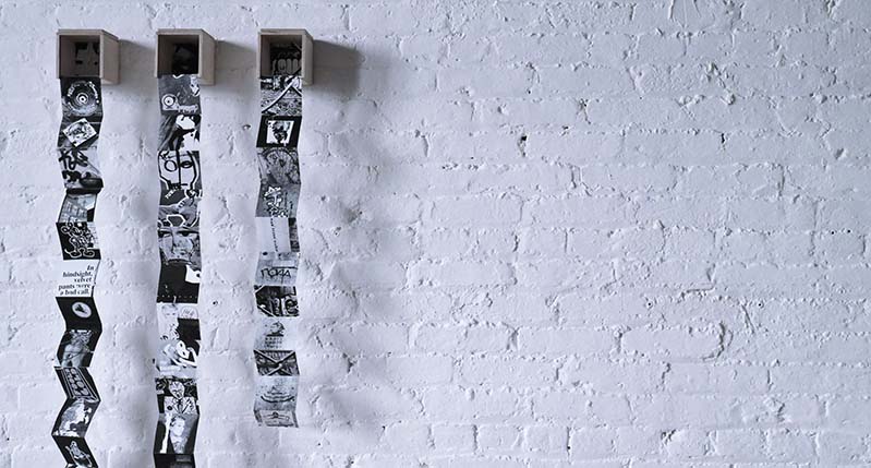 A photo of a white brick wall and on it there are some wood boxes with some zig zag paper flyers popping from them.