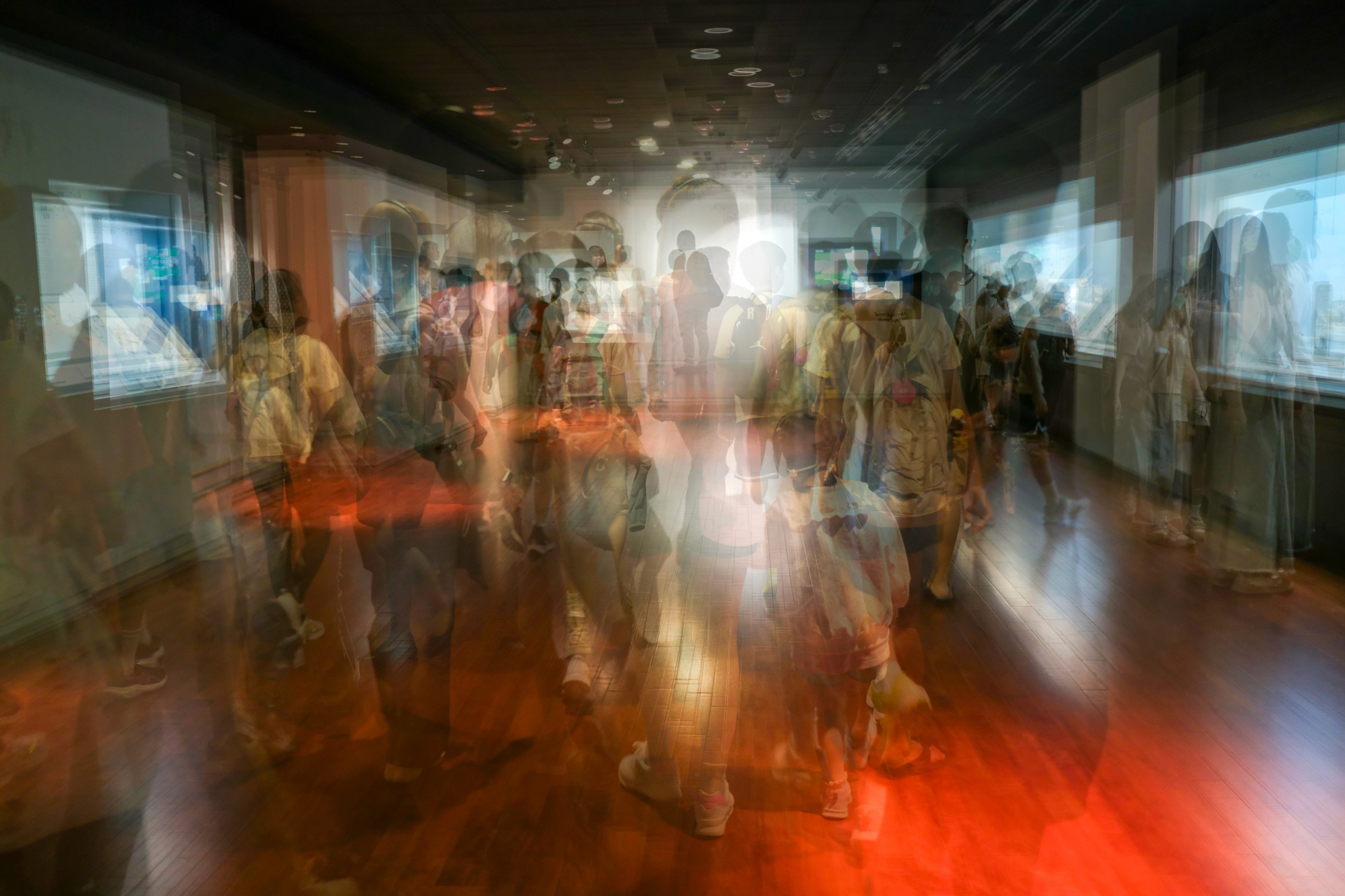 Color abstract motion blur photograph of a large crowd walking through a brightly lit exhibition hall.