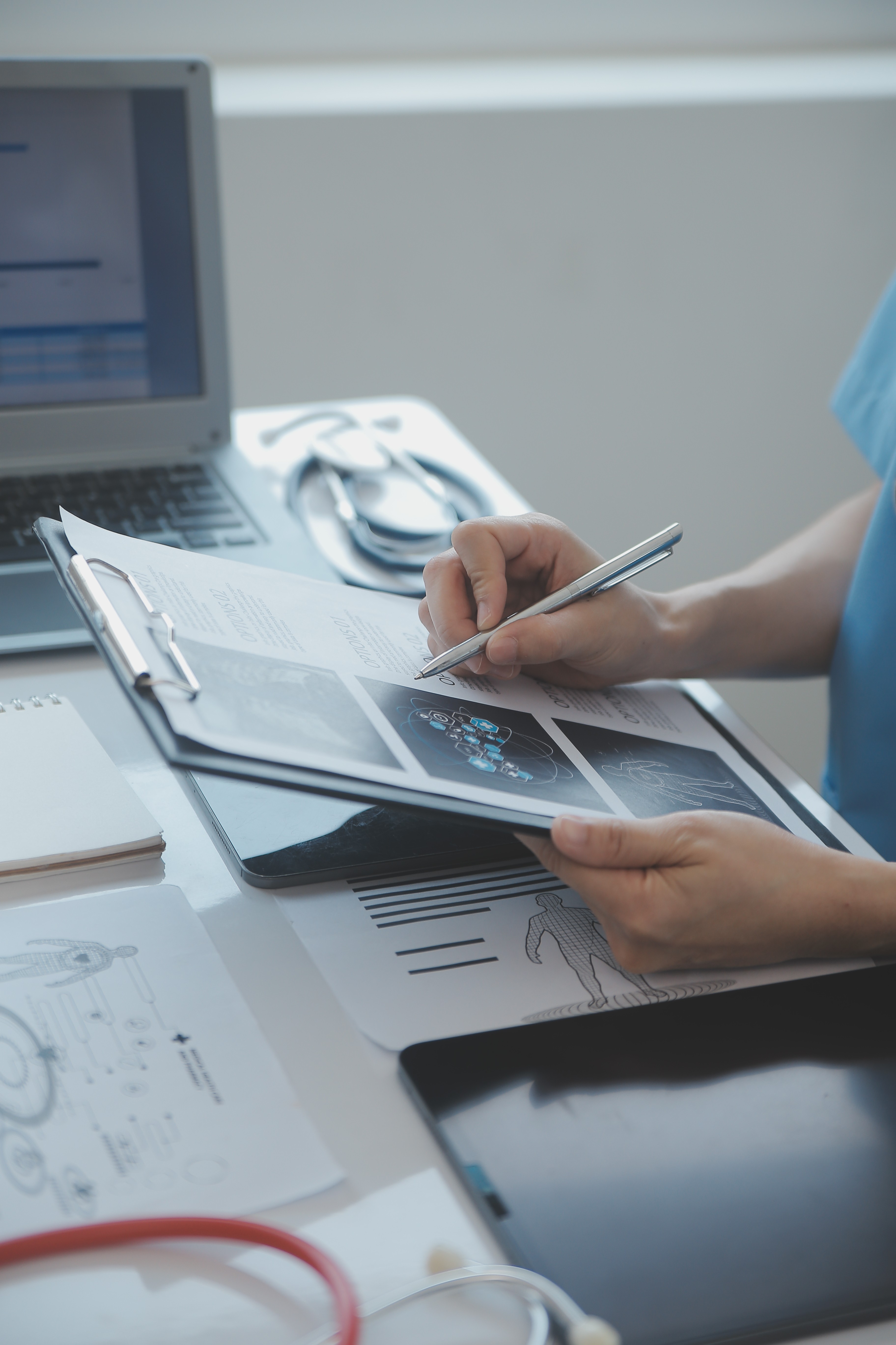 Una persona sosteniendo un portapapeles con documentos médicos impresos en un entorno de oficina, rodeada de tecnología.