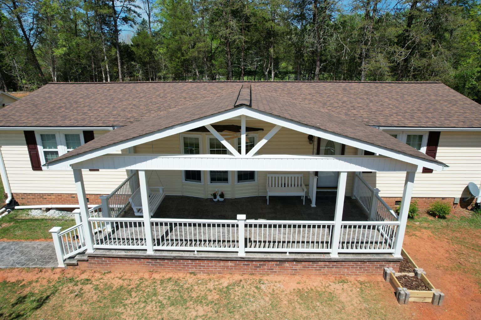 Completed stamped concrete front porch with vaulted gable roof, brick veneer skirting, and Trex railings in Lewisville NC.