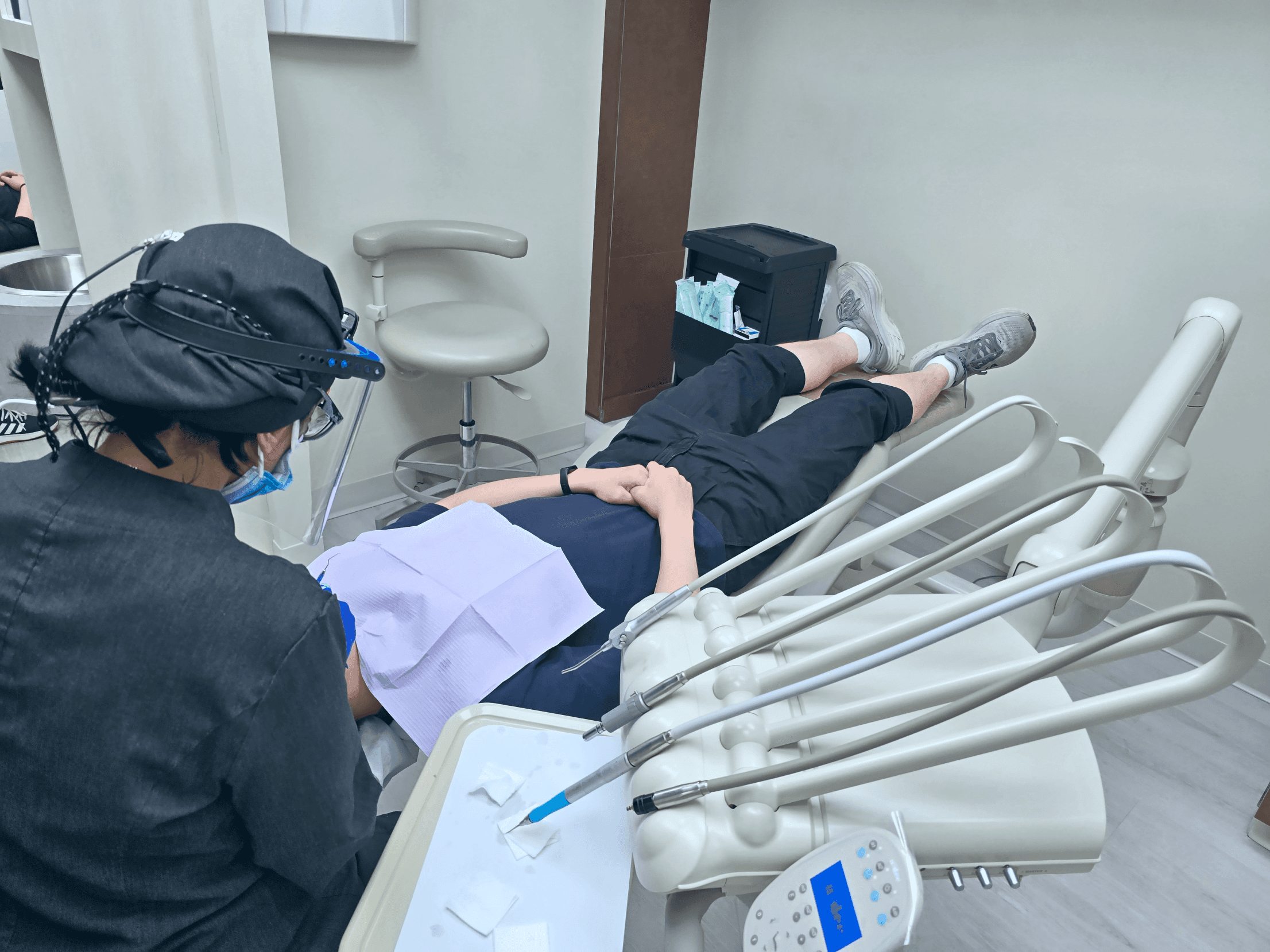 A dental professional wearing protective gear performing a dental procedure on a patient lying in a dental chair.