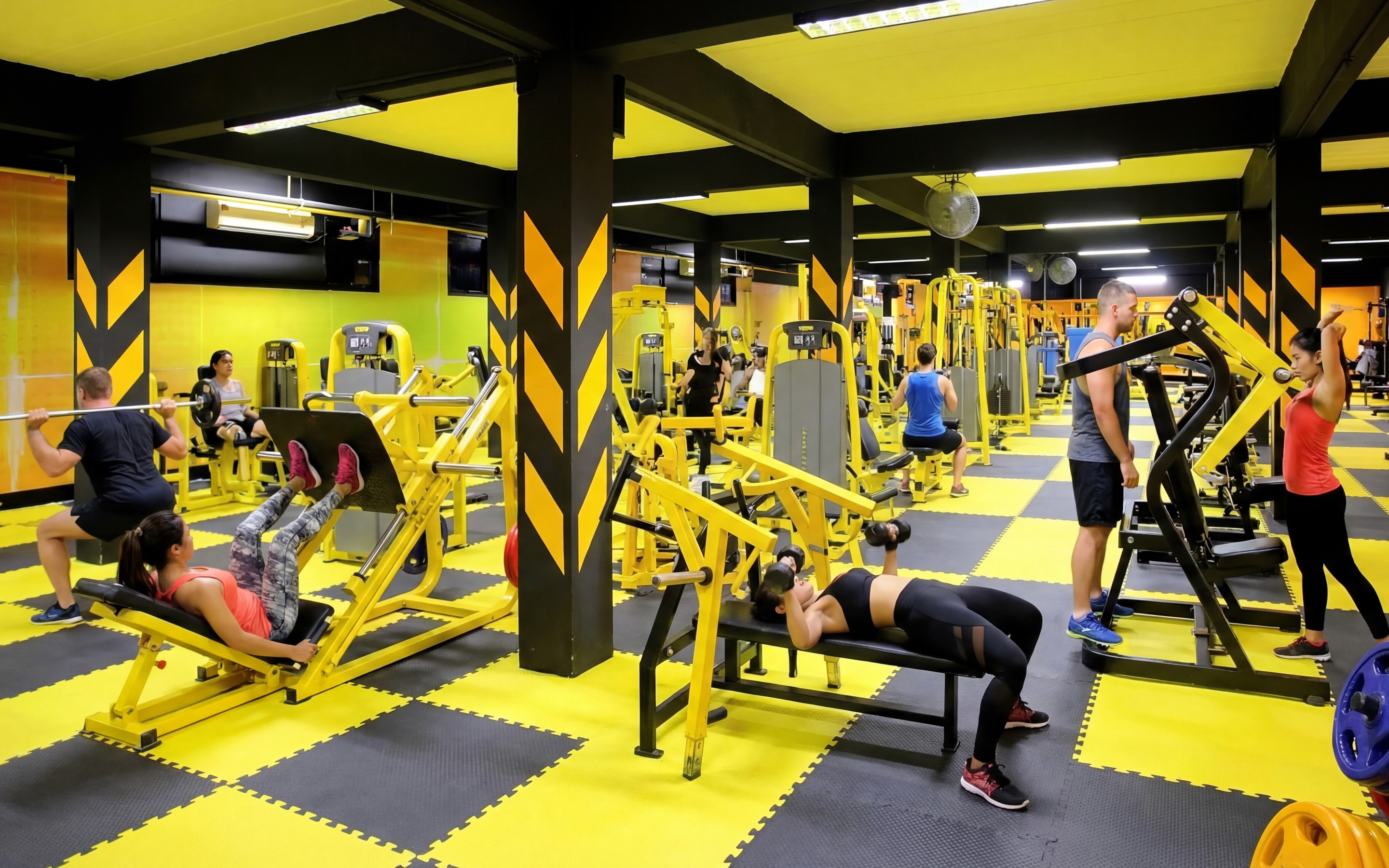 Indoor gym in Krabi with people exercising on weight machines and free weights.