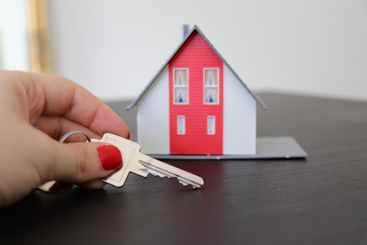 Someone holding a key on a table in front of a small cardboard house 