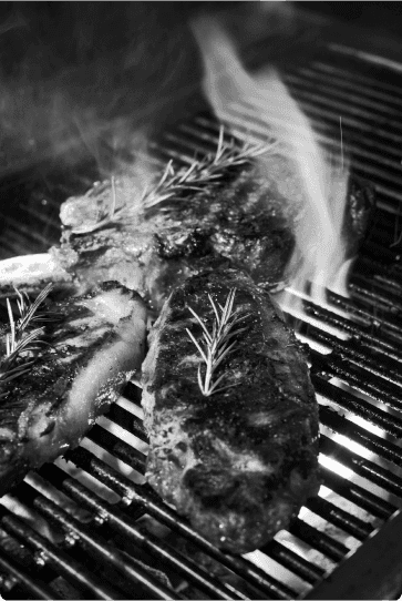 Grilled steak with rosemary on top, sizzling over an open flame.