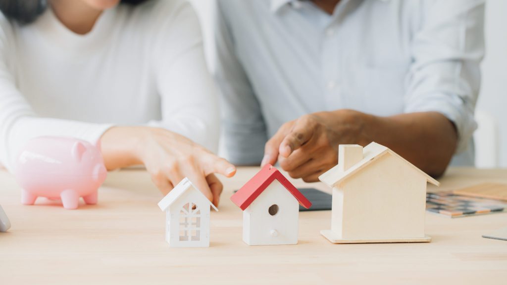 Miniature houses, piggy bank, and hands pointing.