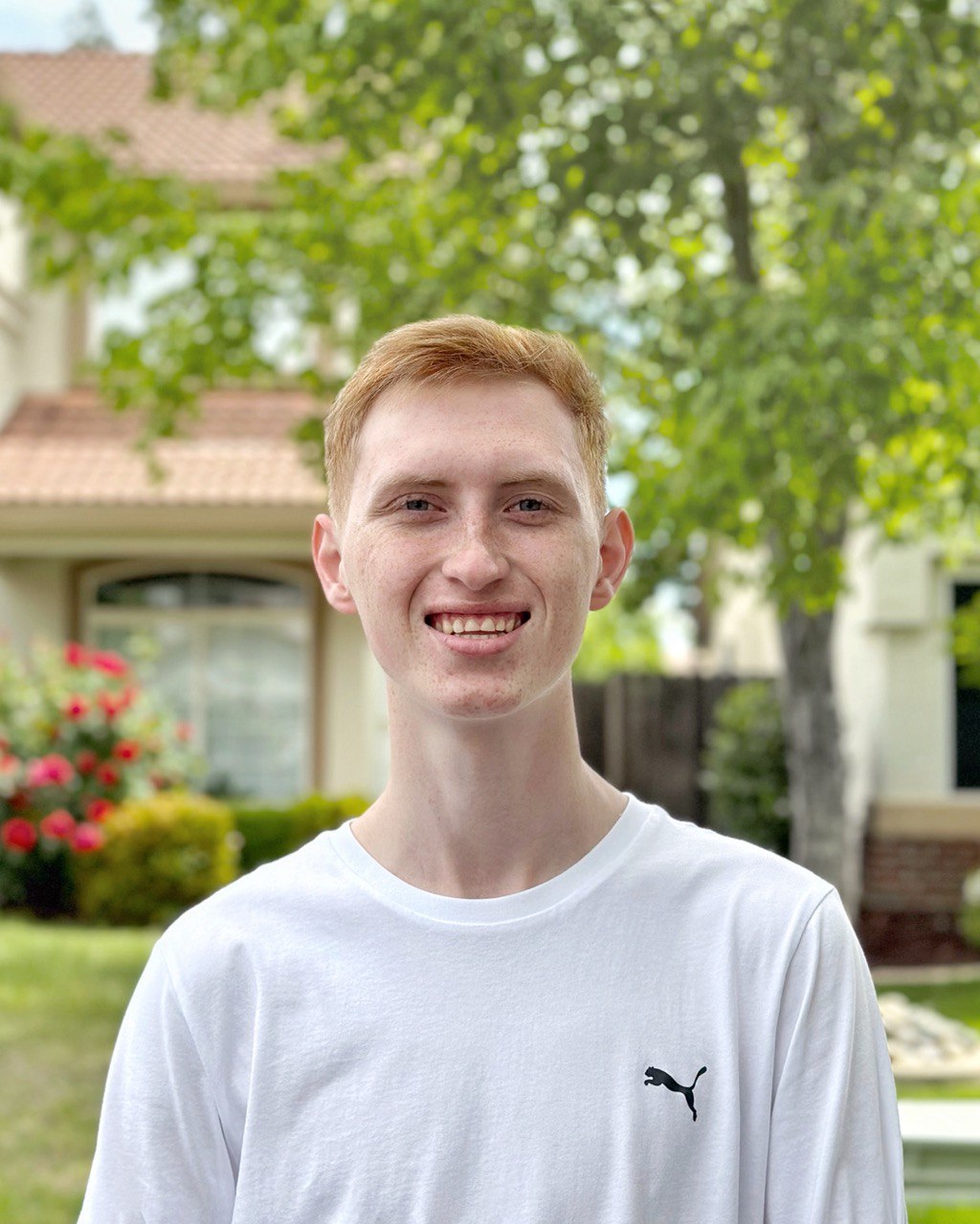 A person with wavy light hair stands facing slightly to the left, wearing a striped shirt against a neutral background.