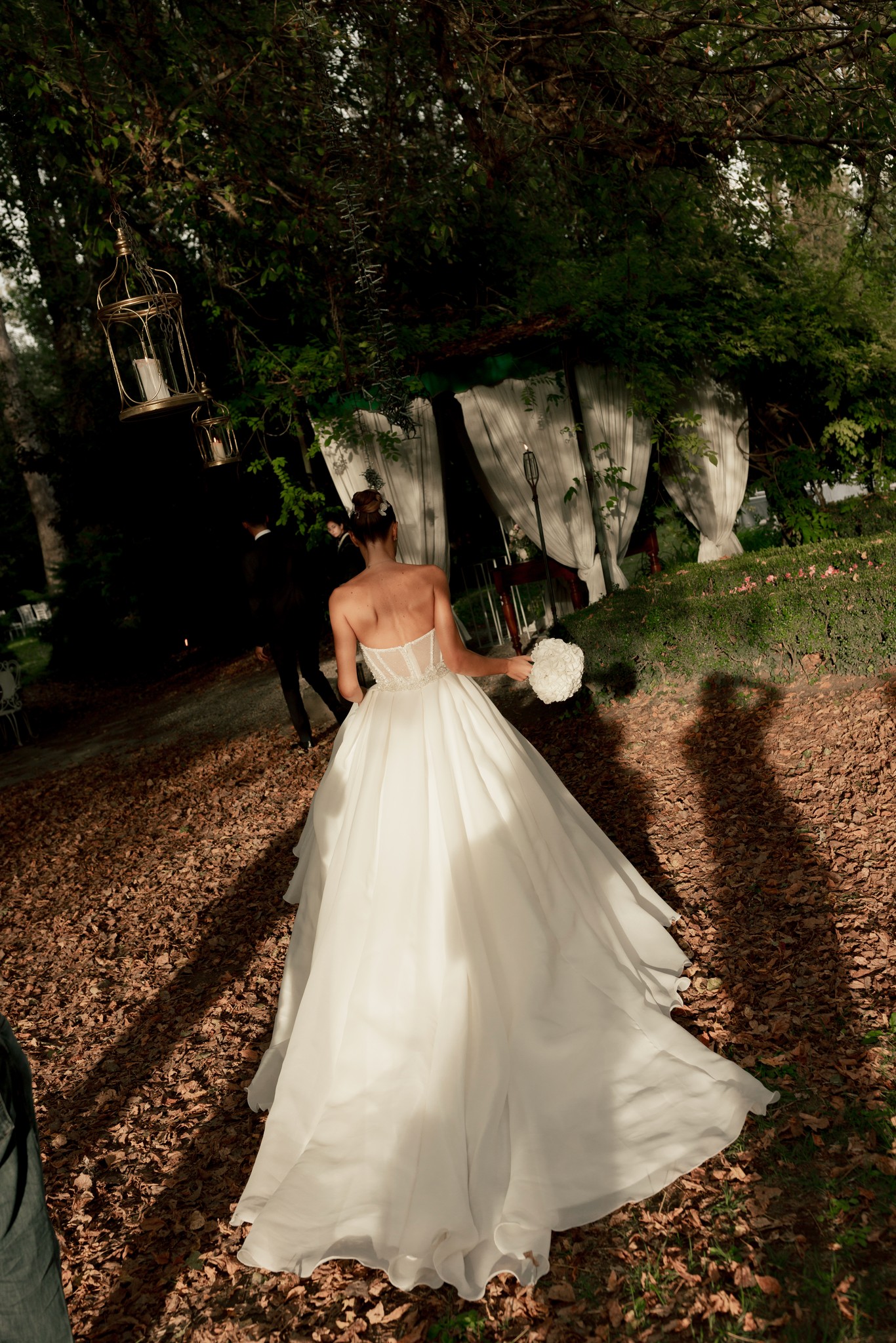 Sposa in abito bianco a Villa Ferrari con velo lungo, cammina tra gli alberi del parco durante i preparativi di matrimonio