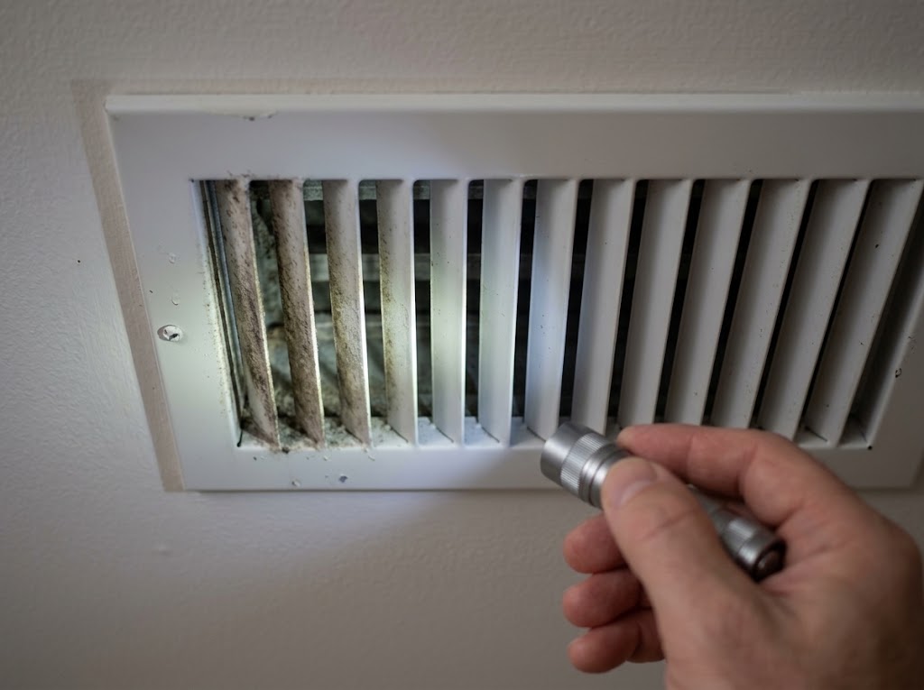 Homeowner using a flashlight to inspect a ceiling air vent register for signs of mold in a Florida home