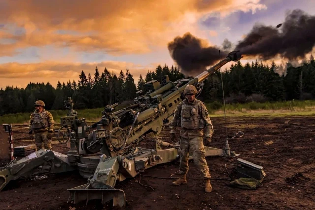 M777 howitzer crew firing at sunset