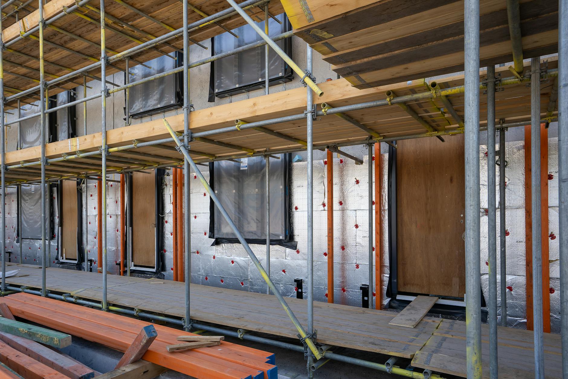 Building under construction showing silver insulation panels fixed to a timber-framed wall with orange scaffolding