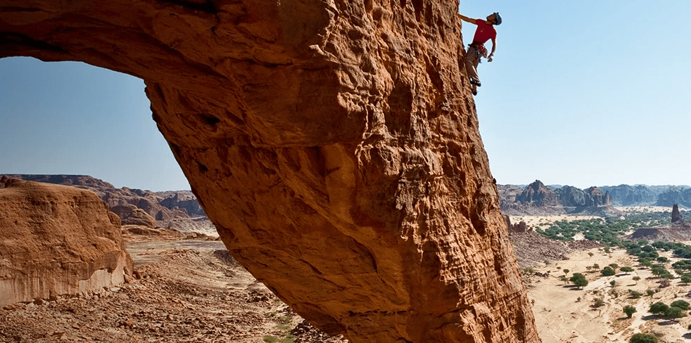 A climber pauses on a rock face to visualize their route on a unique rock formation in the country of Chad in northern Africa.