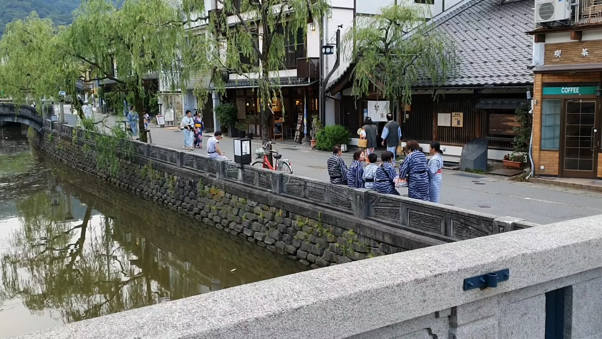 Visitors in yukata crossing a stone bridge over the Kinosaki canal in summer.