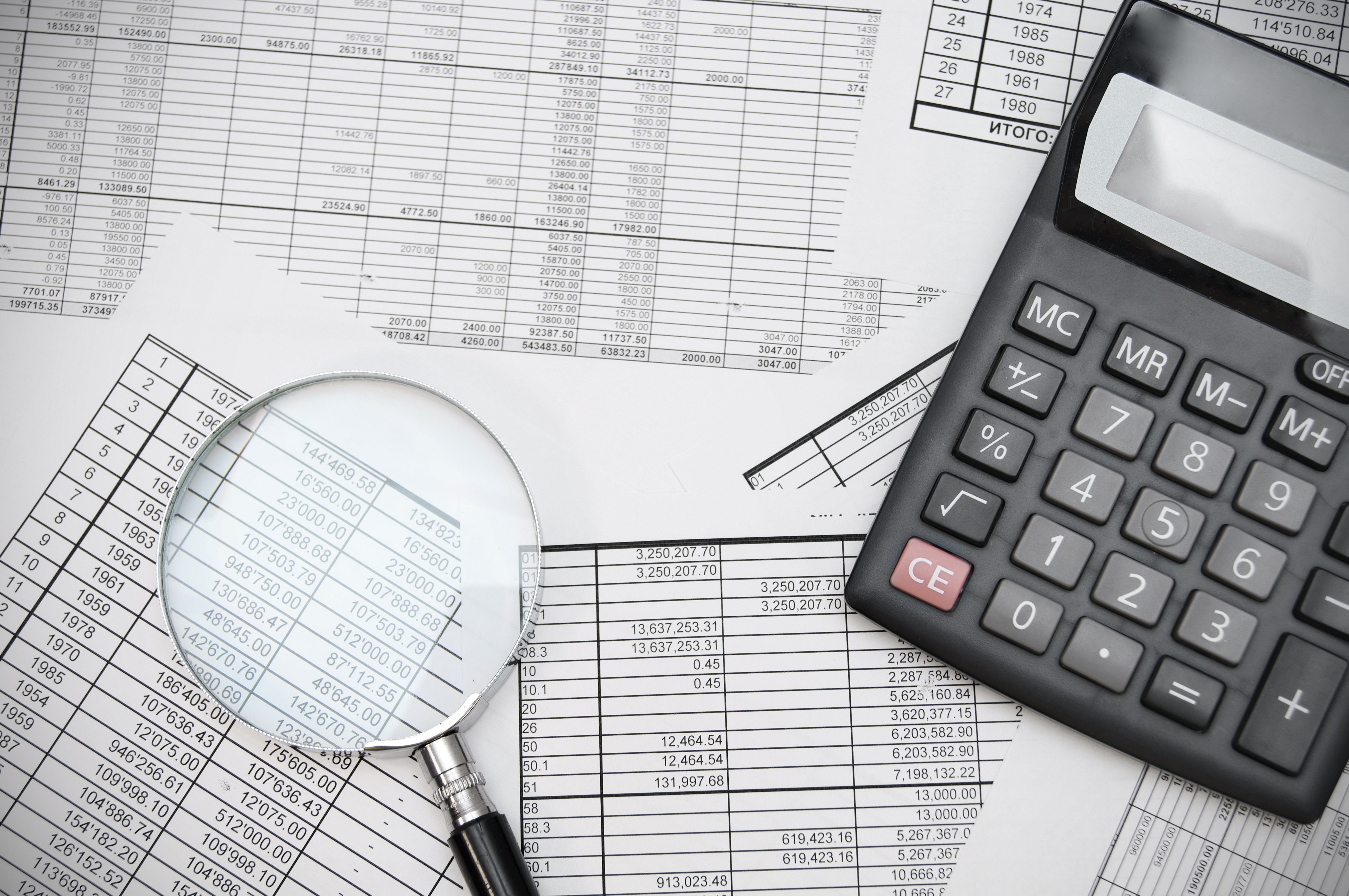 A calculator and magnifying glass resting on printed tables of financial figures.