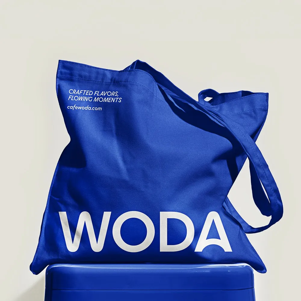 Blue Woda tote bag with white logotype on a blue stool, restaurant brand merchandise