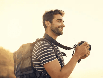 Viajante com mochila e câmera apreciando paisagem ao pôr do sol