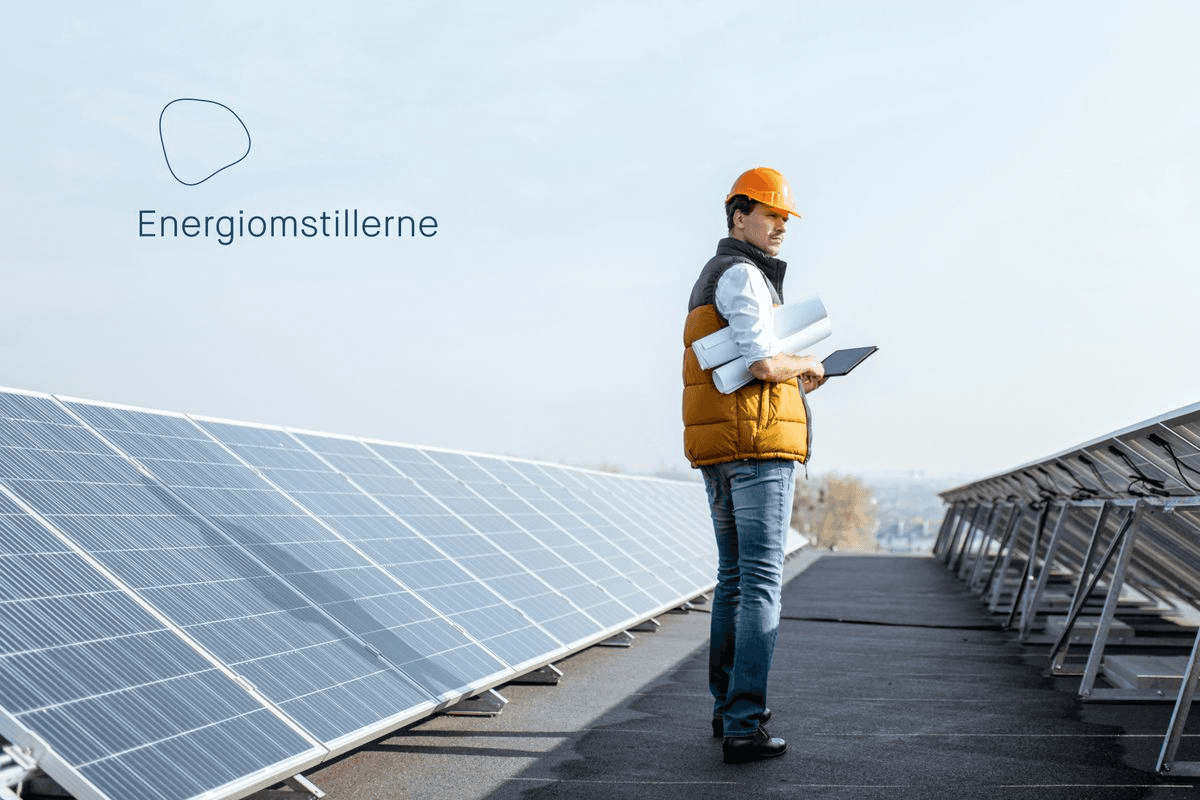 A person in a safety vest and hard hat stands on a rooftop, inspecting solar panels.