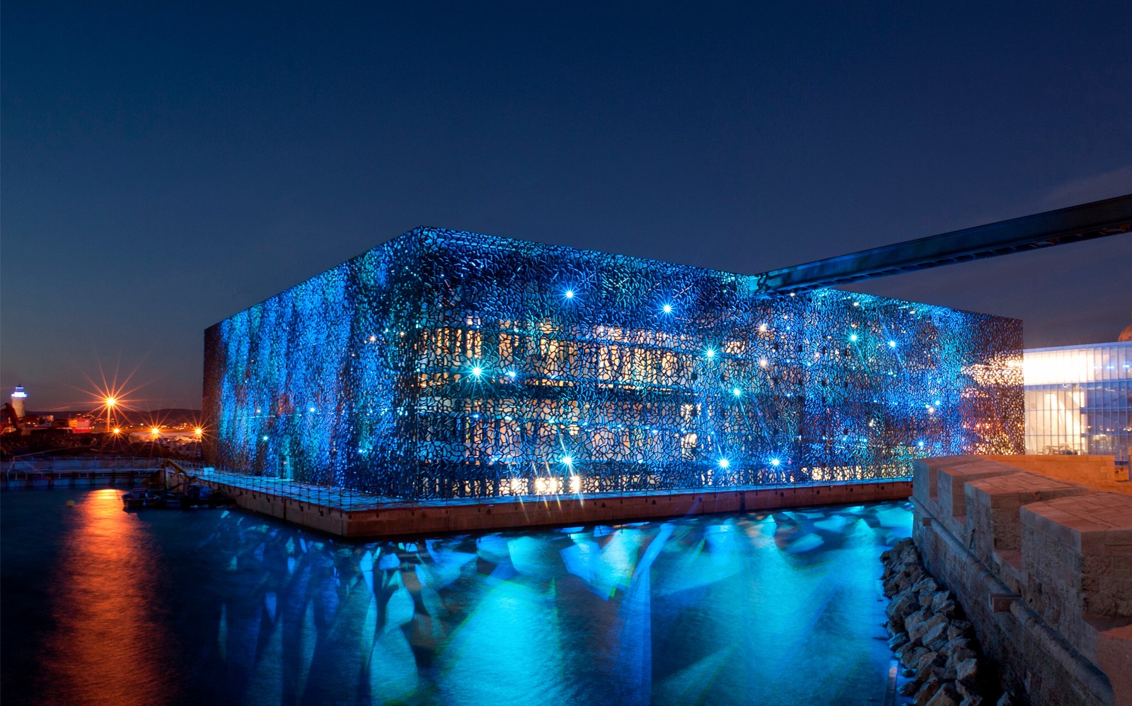 Het Mucem in Marseille, verlicht in de nacht, weerspiegelt op het water.