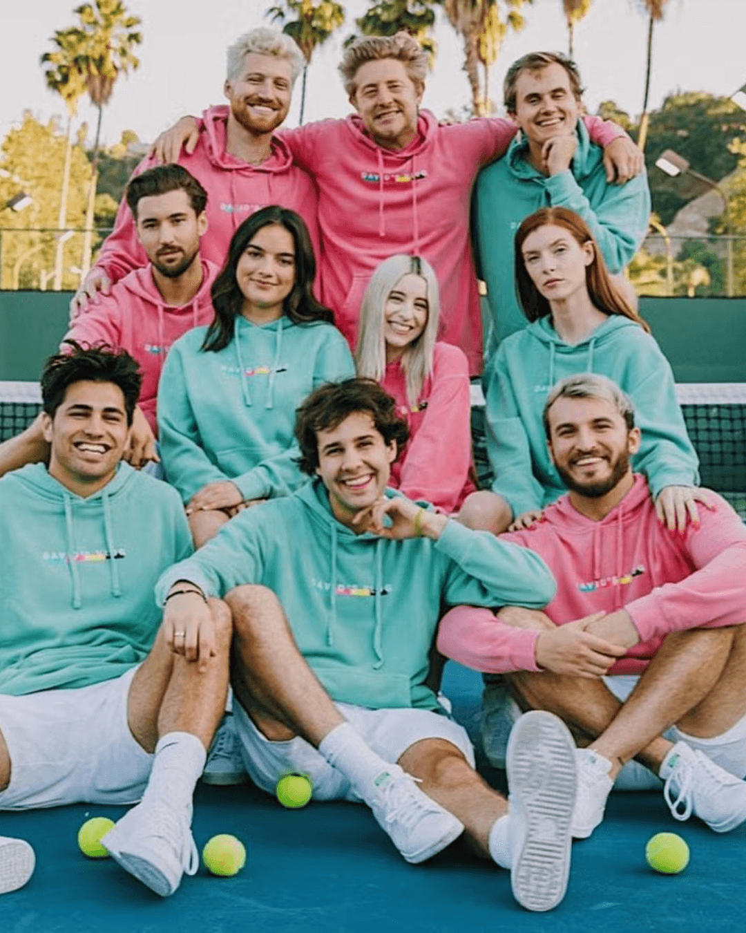 A group of young adults in colorful sweatshirts poses together on a tennis court, smiling and having fun.