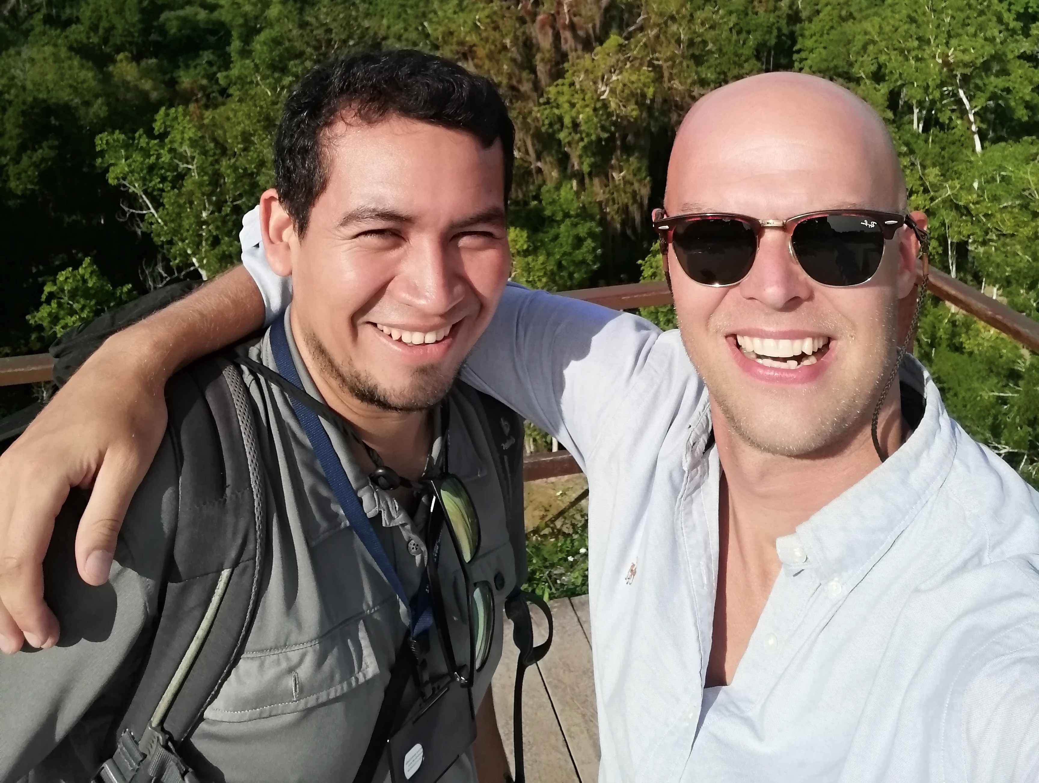 Dos hombres sonriendo para una selfie frente a un bosque.