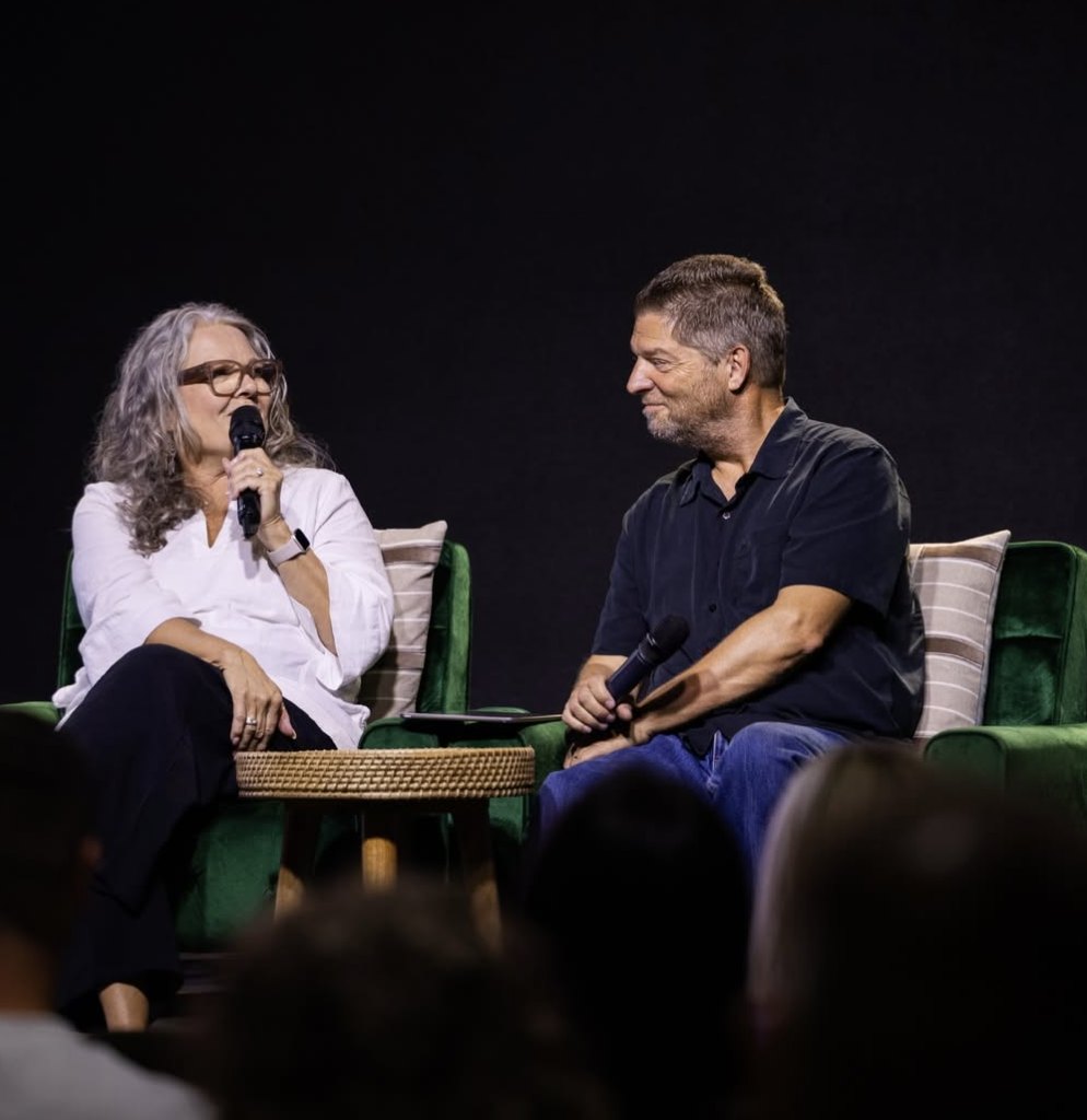 Phyllis Hill speaking into a microphone beside Dr. Glenn Hill on stage