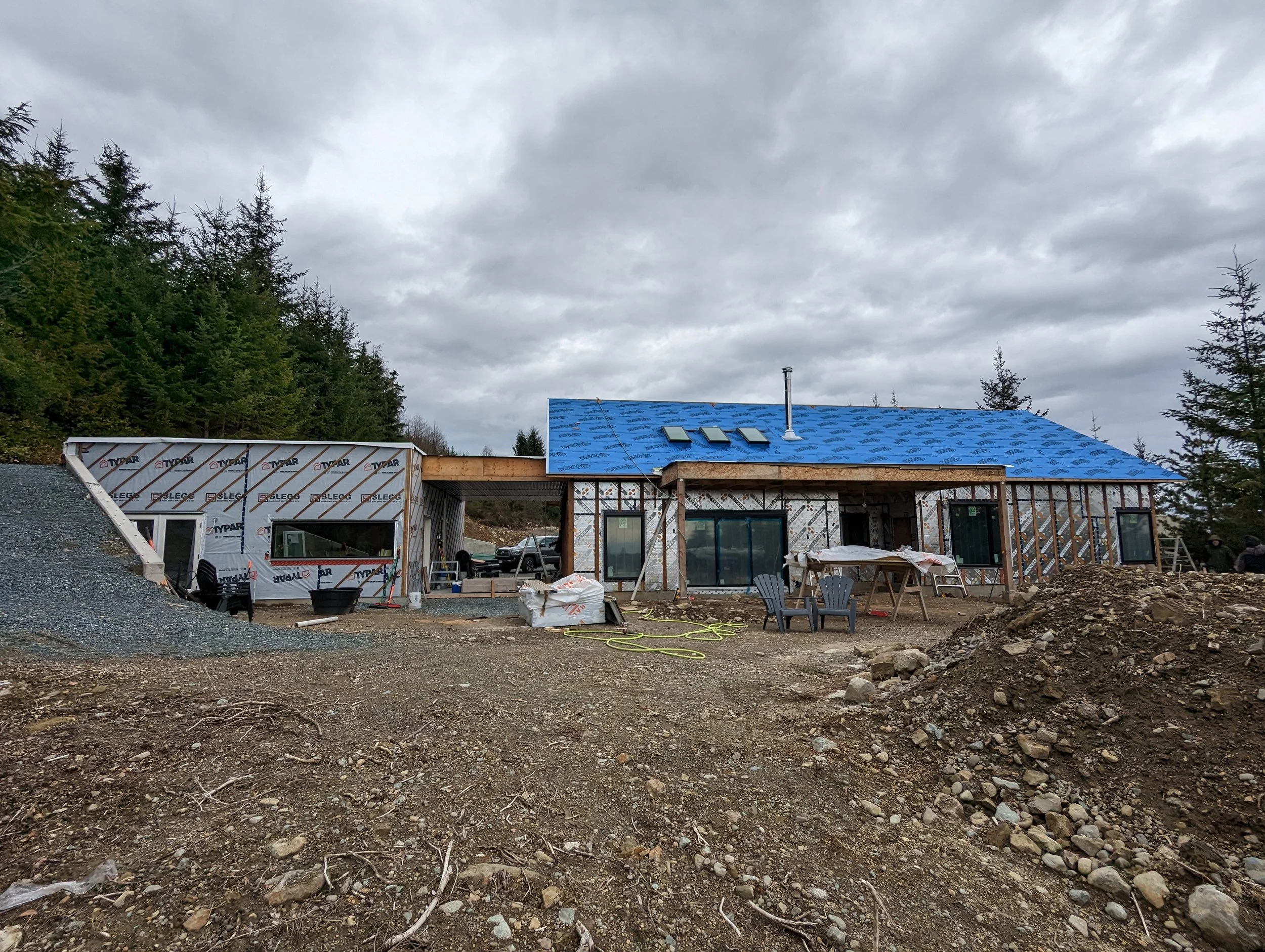 Modern two-story home with large glass windows, warmly lit interiors, and a balcony. Surrounded by trees and a manicured lawn at dusk. Cozy ambiance.