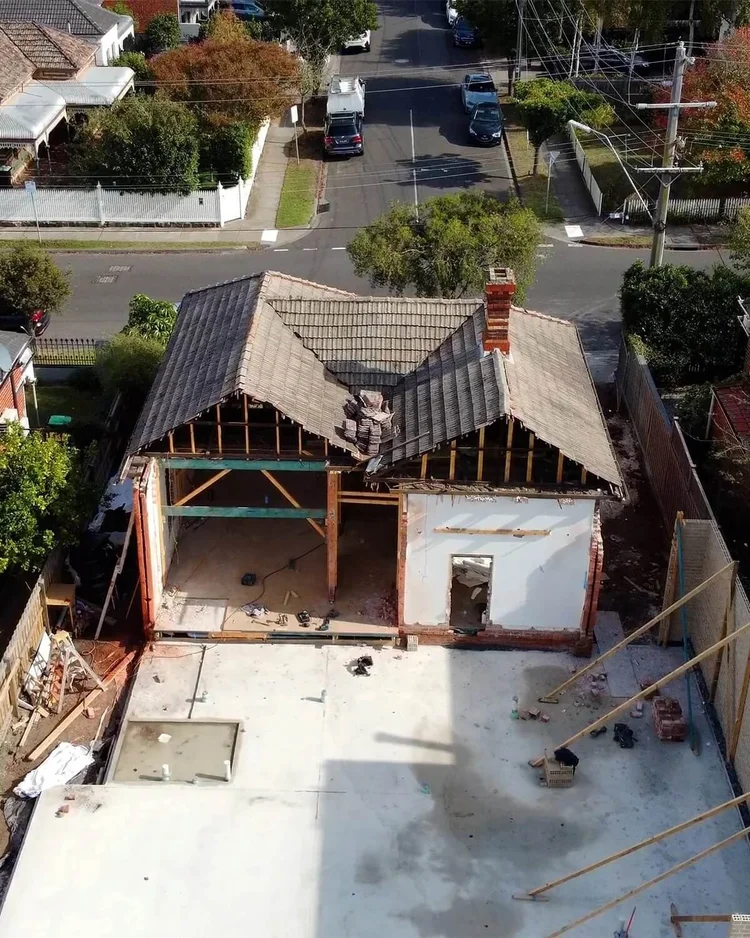 House demolition site with partially intact roof, showing construction progress in suburban neighborhood.