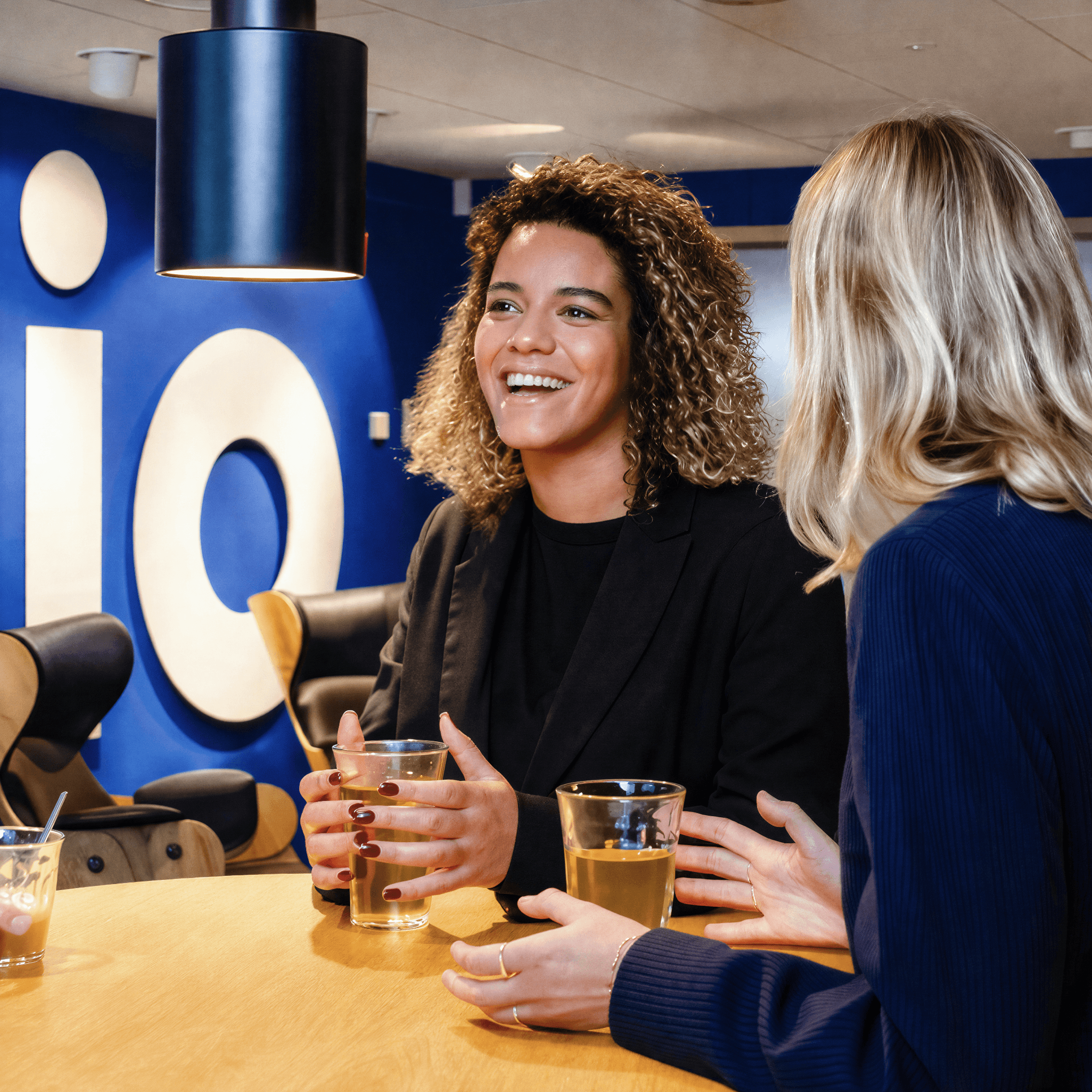Twee vrouwen in gesprek aan een hoge tafel in een sfeervolle ruimte.
