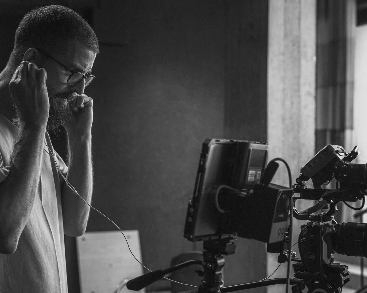 Close-up portrait of a person wearing a gray insulated hooded jacket with the hood up, showing their face framed by the hood against a light background.