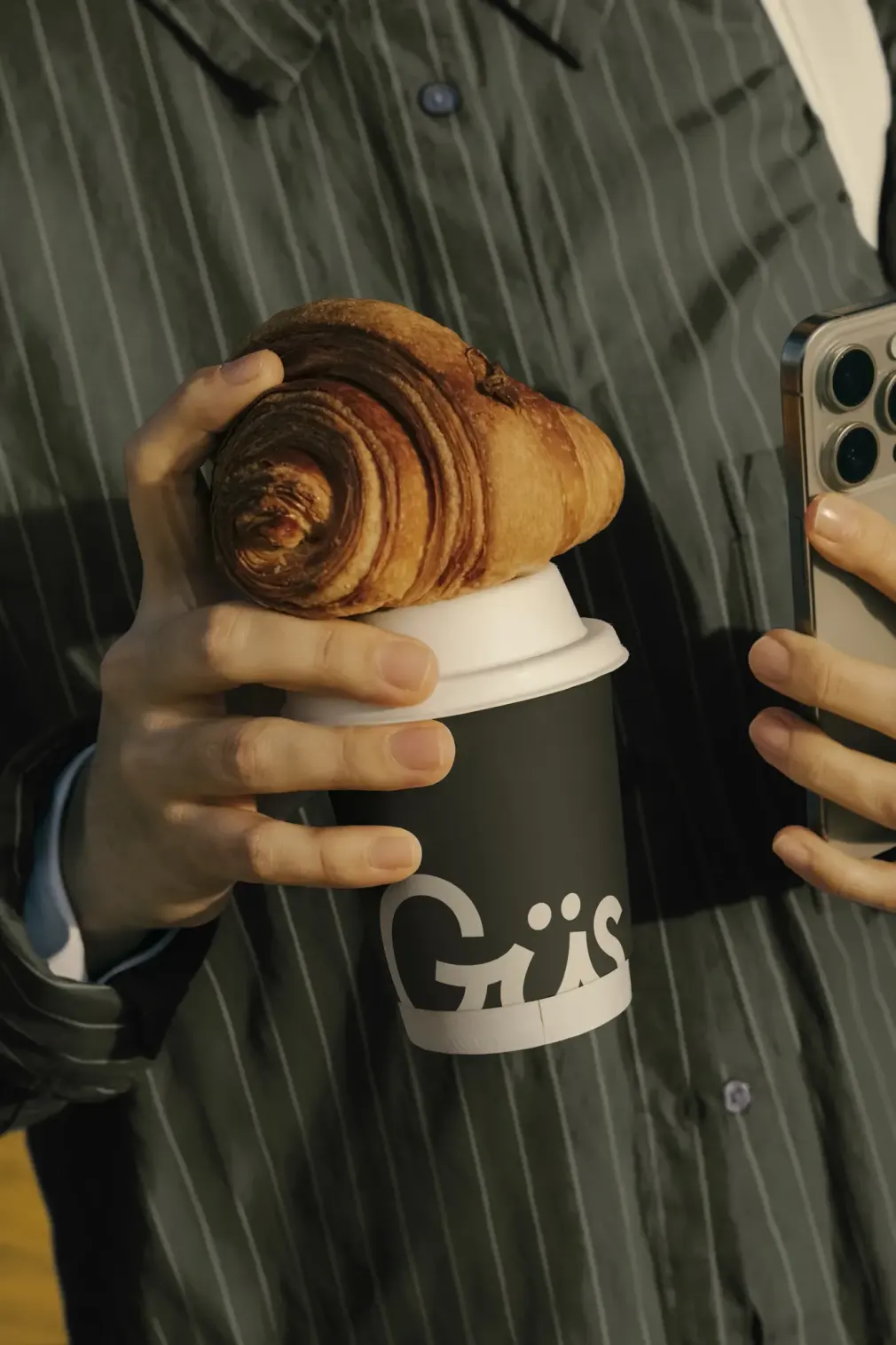 Person holding a Gus coffee cup and croissant