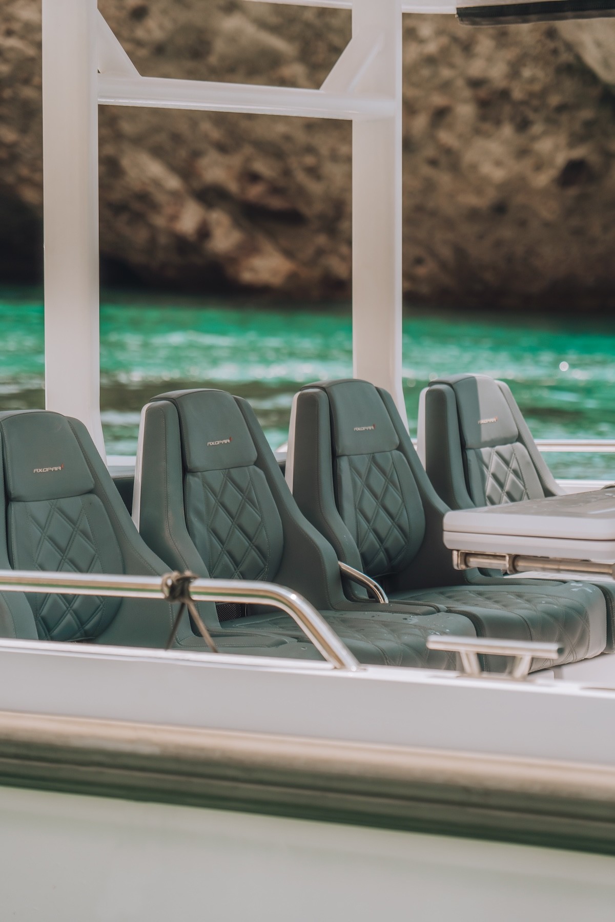 Luxury quilted seating aboard Axopar 37 yacht with turquoise Mediterranean waters and rocky coastline in background.