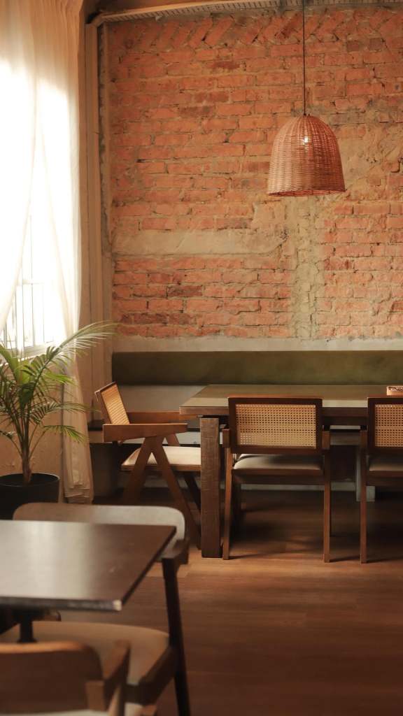 Cozy dining area with a wooden table and chairs, featuring a rustic brick wall and a rattan pendant light.