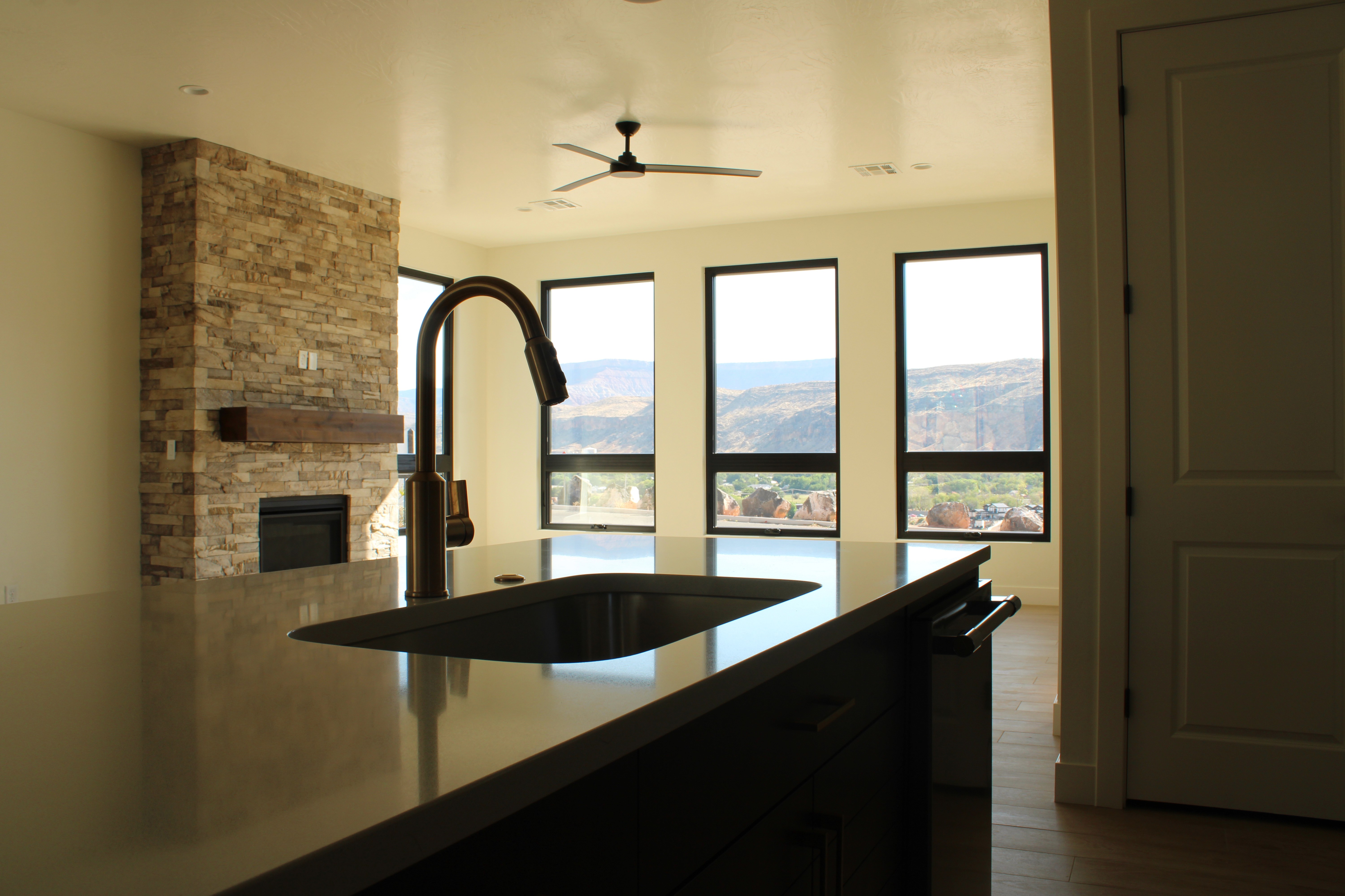 Kitchen of The Overlook at Falcon Ridge in Hurricane, Utah, featuring dark stained wood cabinetry, bronzed gold hardware, and large windows with valley and mountain views.