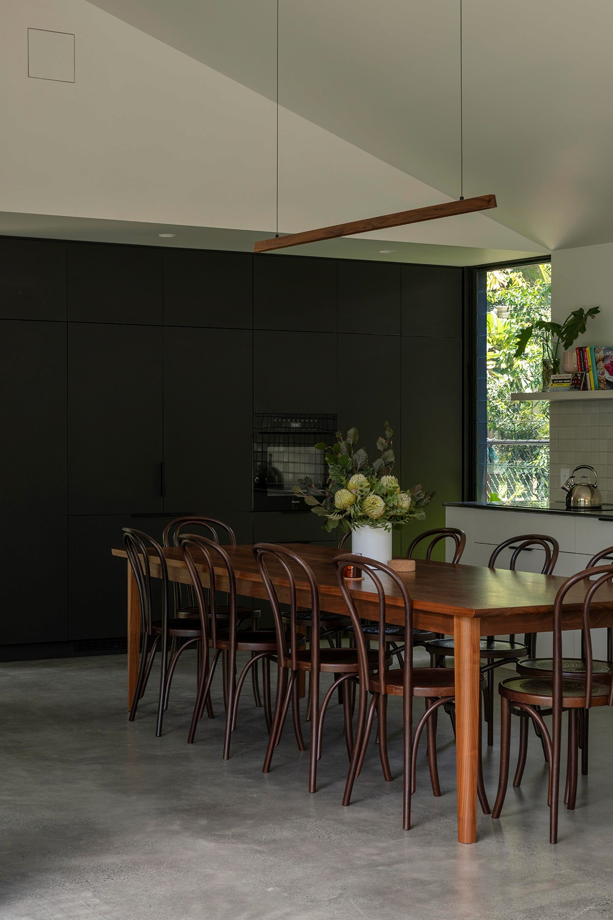Dining area at Toohey Forest House with timber table, bentwood chairs, and contemporary kitchen backdrop.
