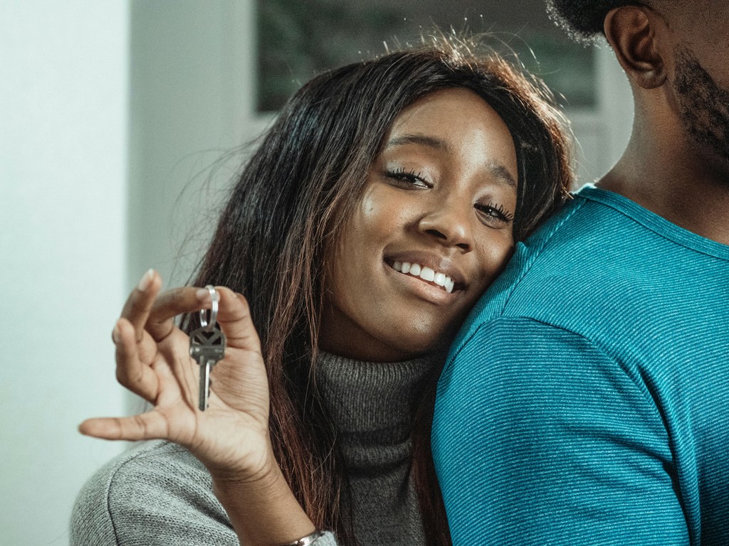 A smiling newcomer to Canada holding up the keys to her new apartment, representing the reality of economic immigrants successfully securing and paying for their own housing in the Canadian rental market.