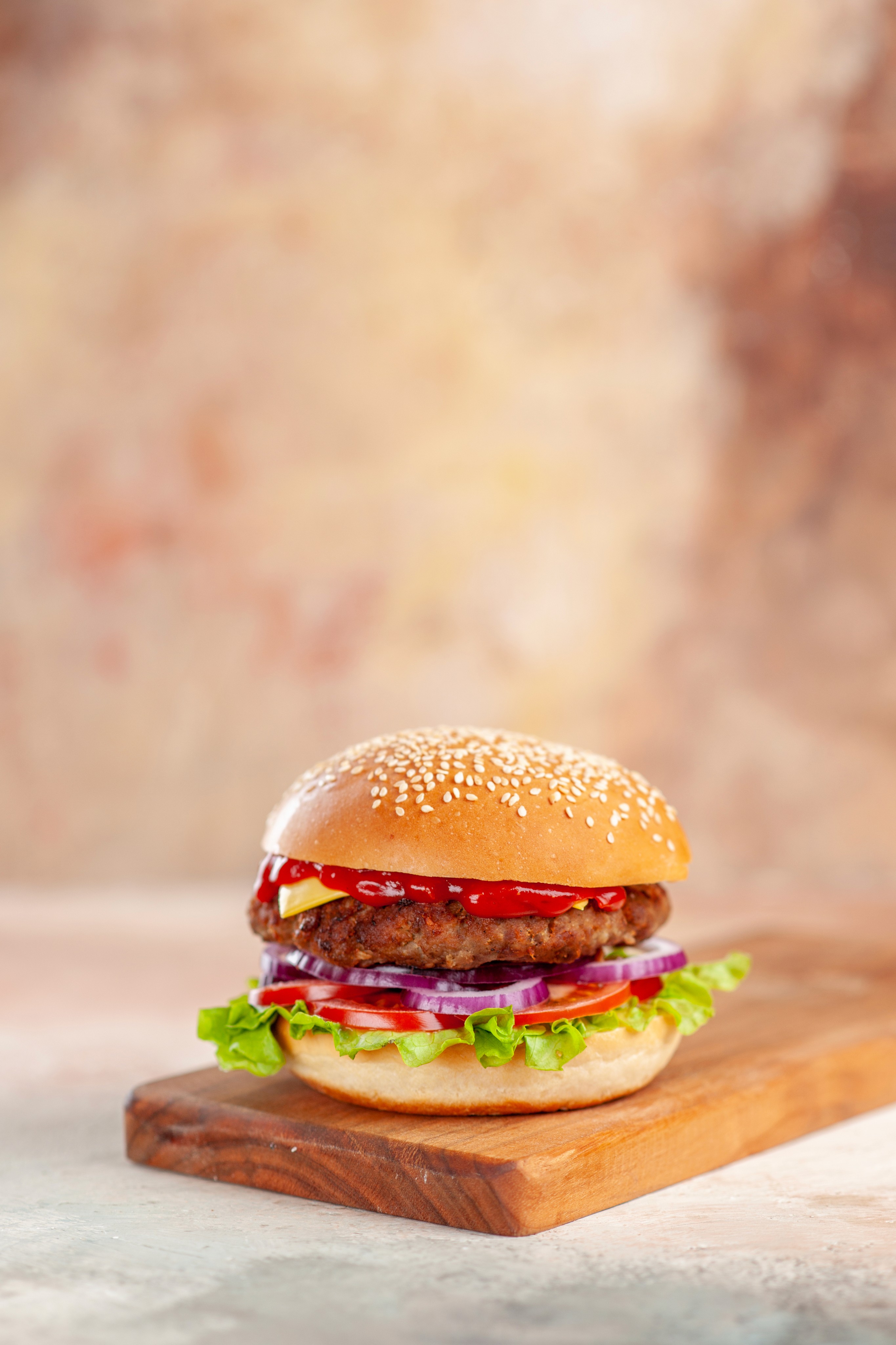 A juicy cheeseburger with lettuce, onion, tomato, cheese, and ketchup sits on a wooden board with a blurred background, conveying a fresh and appetizing appeal.