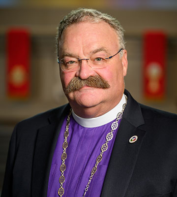 A young man with dark hair smiles at the camera, set against a modern indoor background.