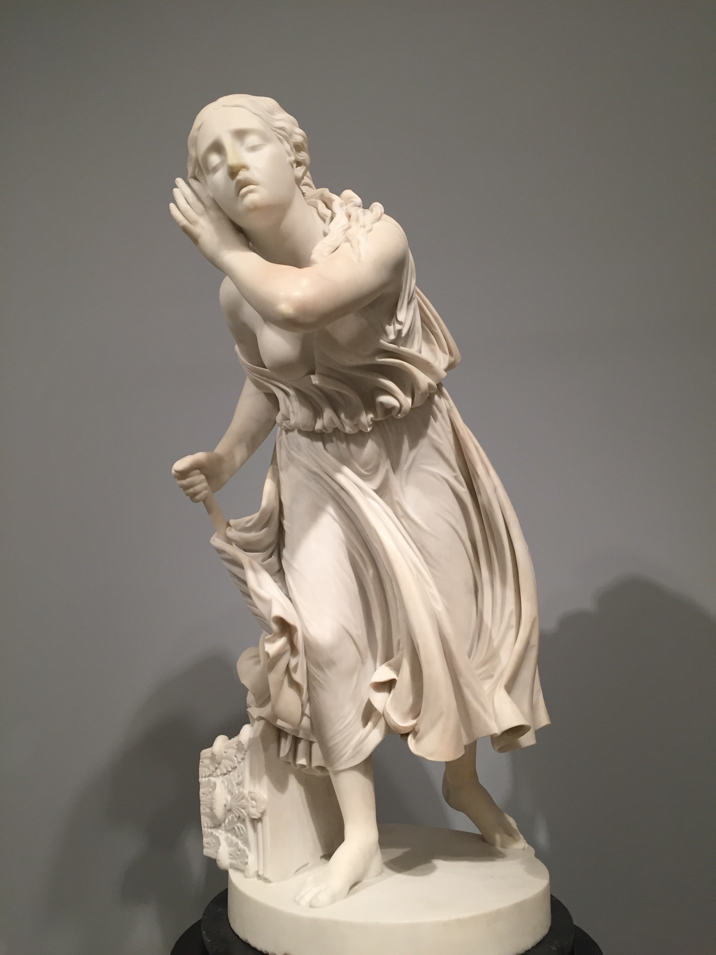 A neoclassical marble sculpture of a woman in flowing robes, eyes closed and hand raised to her head in a dramatic pose
