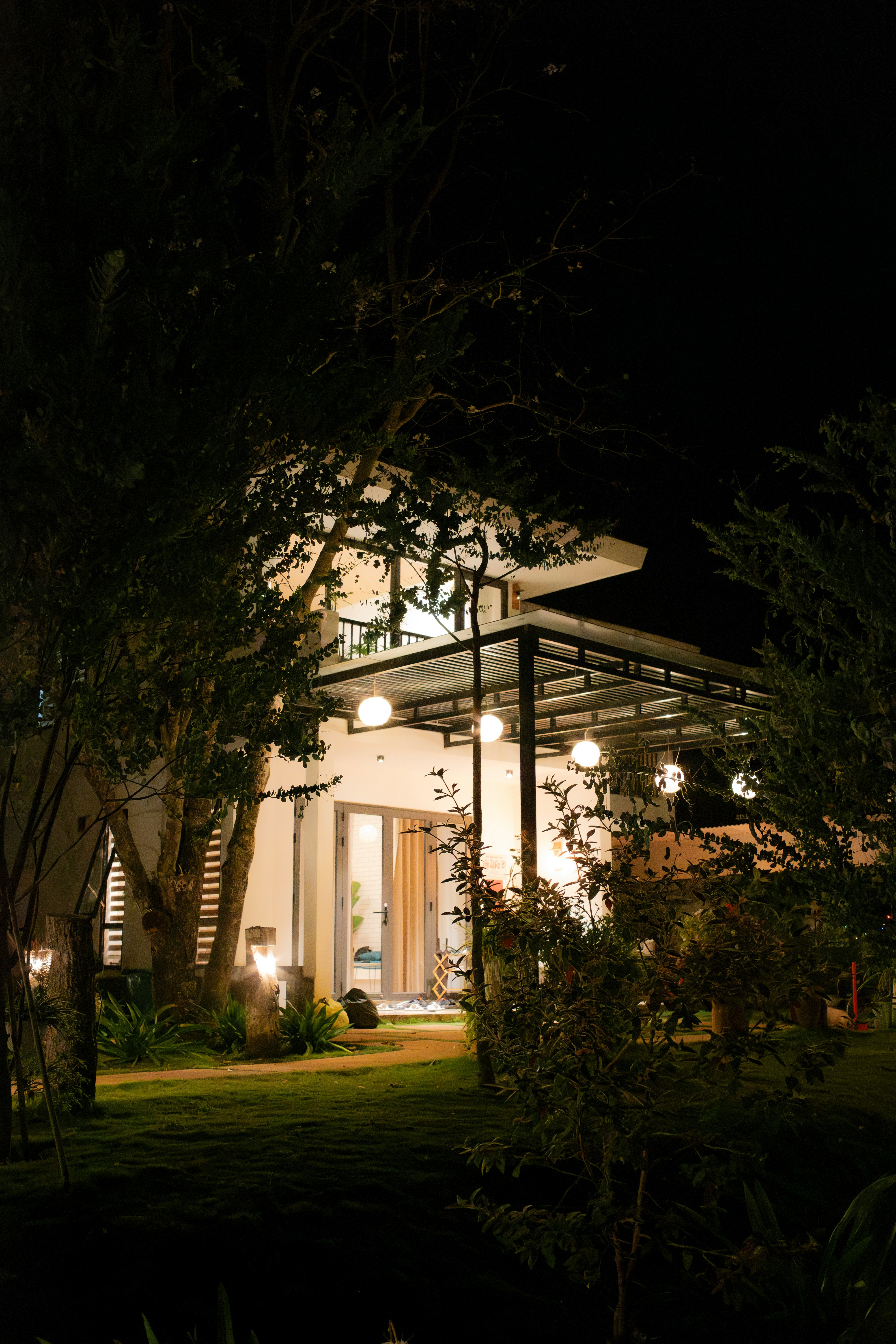 Maison éclairée la nuit avec un aménagement paysager et des lumières extérieures chaleureuses.