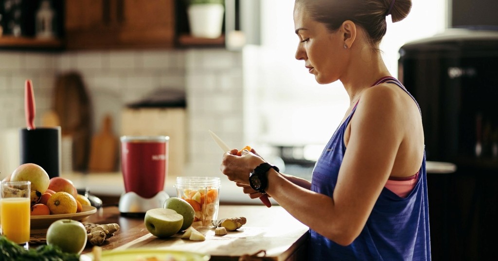 Post-exercise nutrition: woman in a tank top making a healthy smoothie with fruits and vegetables.