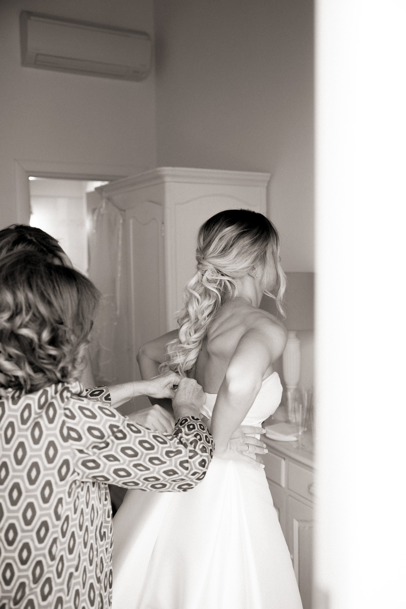 Sposa abbottonata nel vestito bianco da una donna durante i preparativi del matrimonio a Bolgheri, fotografo reportage