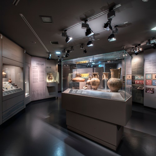 博物馆展览中,一批古代陶器陈列在玻璃展柜内,上方配有聚光灯,并设有信息说明展板。