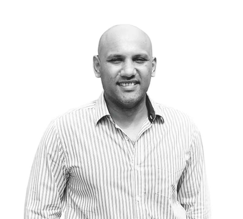 A focused woman with long red hair is seated at a desk, wearing a black blazer and dark blouse. She intently looks at camera, smiling slightly, with an open laptop in front of her. The setting is a warm and serene office setup in the background. Soft daylight filters through, creating a calm atmosphere. The composition captures her in a frontal profile with a clear emphasis on her concentration and the serene indoor setting.