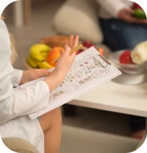 Nutricionista de jaleco branco segurando prancheta durante consulta com frutas ao fundo