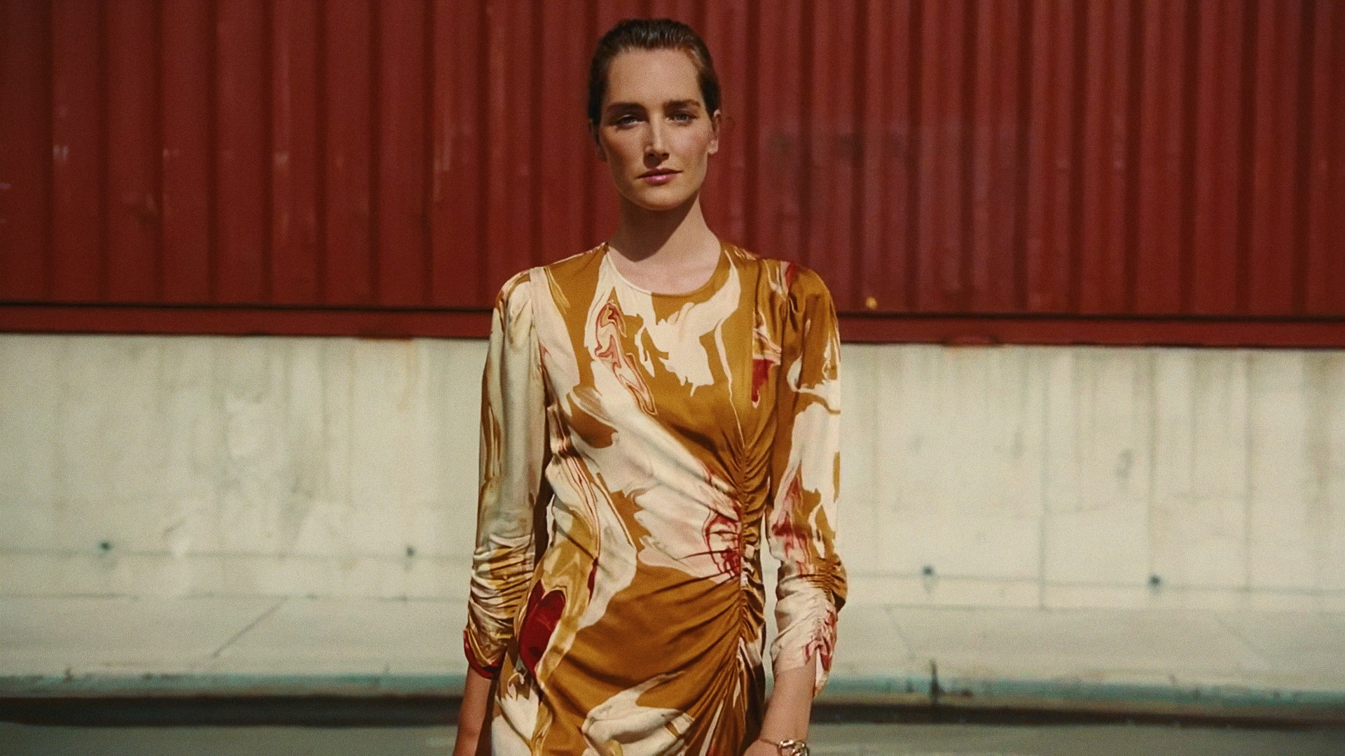 A woman in a gold printed dress in front of red shipping containers, Lafayette 148 New York